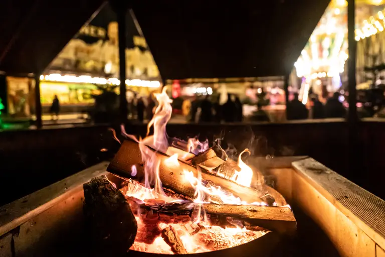 Knisterndes Feuer in der Feuerstelle im Außenbereich, dahinter leuchtet das Gelände