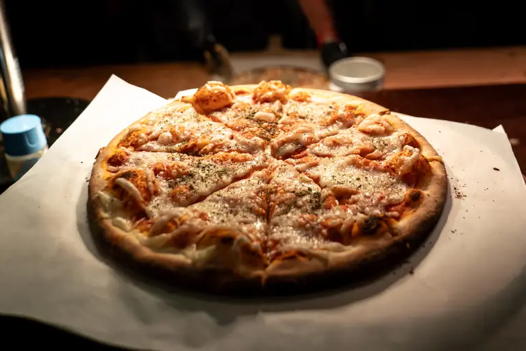 Frisch gebackene Pizza mit geschmolzenem Käse auf Backpapier im Spotlicht