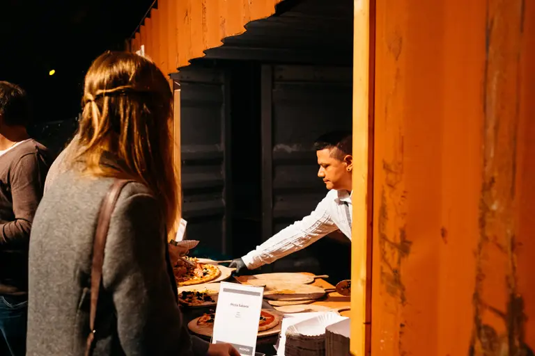 Mitarbeiter reicht eine Pizza über den Tresen des Standes an wartende Gäste