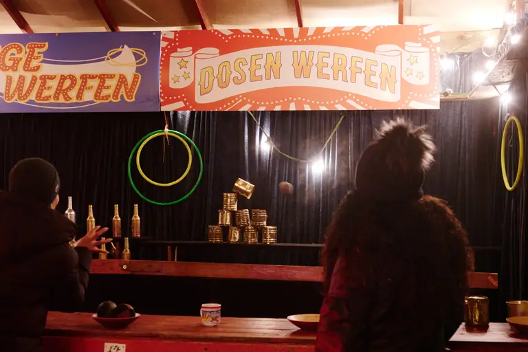 Zwei Besucherinnen werfen an der nostalgischen Bude Bälle auf goldene Dosen