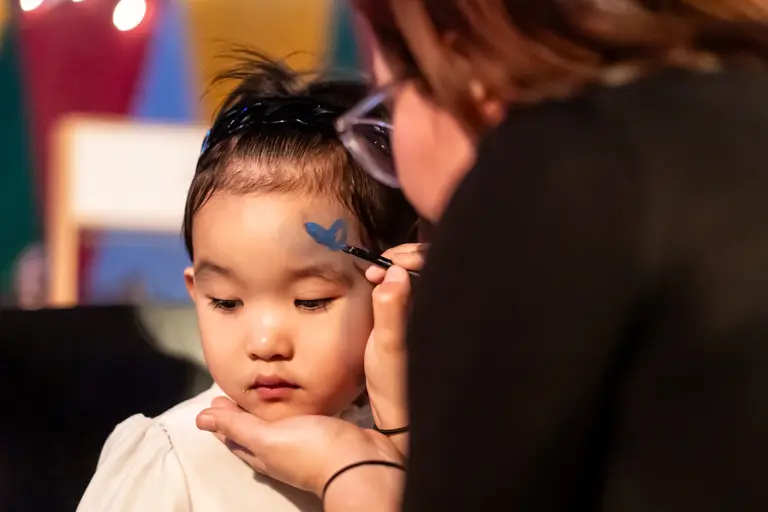 Ein Kind bekommt beim Kinderschminken im Kinderparadies einen blauen Schmetterling auf die Wange gemalt