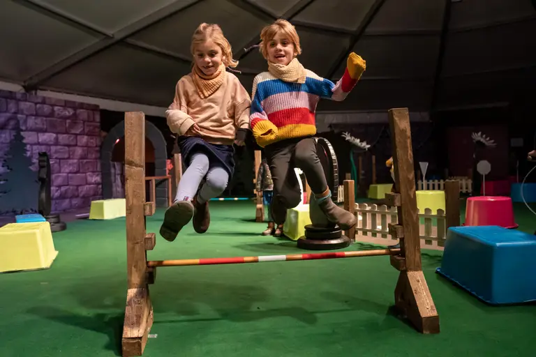 Zwei Kinder springen lachend über Hindernisse im Parcours des Kinderparadieses