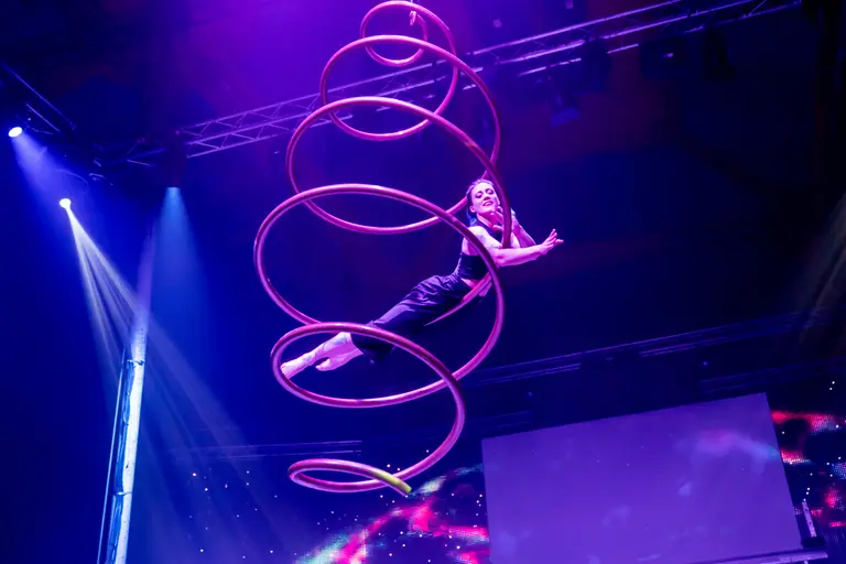 Artistin wirbelt in einer Spirale aus leuchtenden Reifen durch das violette Bühnenlicht