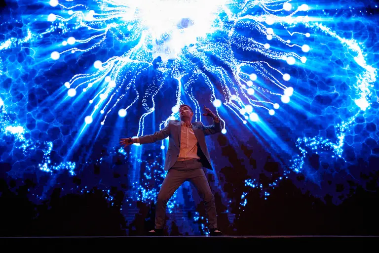 Artist tanzt vor einer riesigen LED-Wand, aus der blaue Lichtfäden wie ein Feuerwerk explodieren